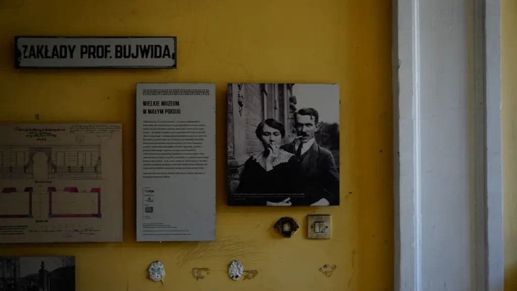 Archiwalne fotografie i dokumenty historyczne prezentowane na żółtej ścianie w polskim muzeum.