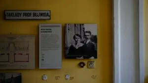 Archiwalne fotografie i dokumenty historyczne prezentowane na żółtej ścianie w polskim muzeum.