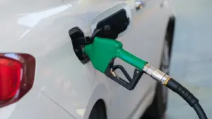 Pistolet dystrybutora paliwa wlewa benzynę do baku białego samochodu osobowego na stacji.