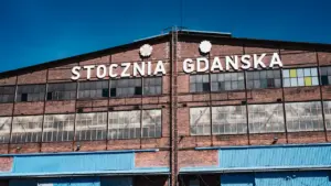 Historyczny budynek Stoczni Gdańskiej z napisem na tle czystego, błękitnego nieba.